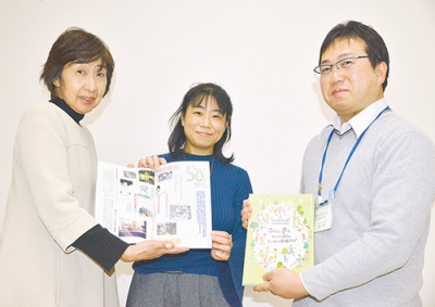 写真：活センで石崎主任（右）に５０周年記念誌を手渡す（左から）泉田実行委員長と佐藤運営委員長