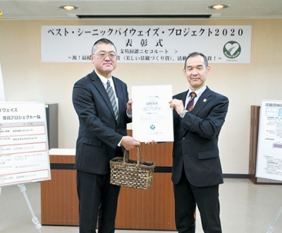 写真：最優秀賞の表彰状を手に笑顔を見せる三松事務局長（左）と篠宮部長