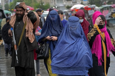 写真：タリバン兵が警備する市場を歩くアフガニスタンの女性。公共の場で女性は顔を布で覆うようタリバンが命令した＝５月、カブール（ＡＰ＝共同）