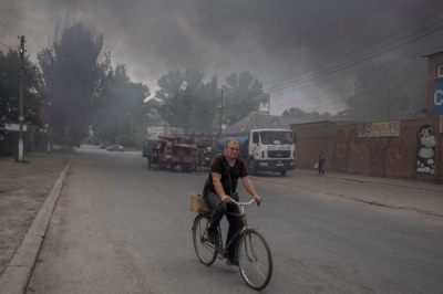 写真：５日、ロシア軍の攻撃により上がる煙の中を自転車で進む男性＝ウクライナ東部ドネツク州スラビャンスク（ロイター＝共同）