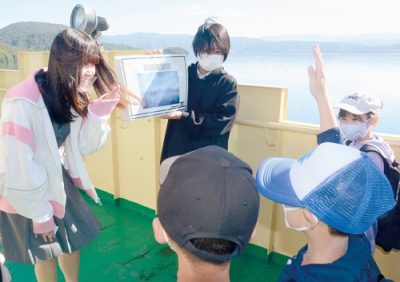 写真：フリップを使いガイドを行う虻田高校の生徒と説明を聞く洞爺湖温泉小の児童