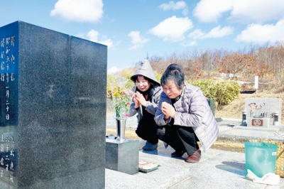 写真：墓前で手を合わせる上出さん（右）と末久さん