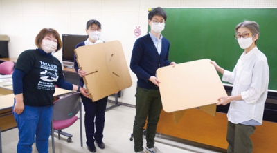 写真：段ボール製のテーブルを寄贈する島川代表（右）と受け取る渡邉さん（左隣）