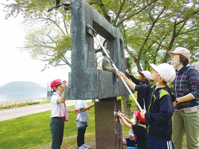 写真：彫刻の清掃活動に汗を流す温泉小児童たち（提供写真）