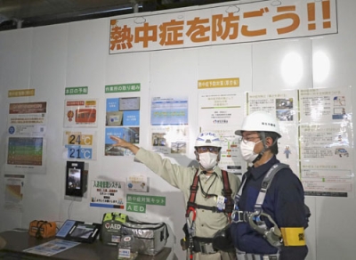 写真：視察に訪れたビル建設現場で、現場責任者（左）から熱中症対策などの説明を受ける愛知労働局の代田雅彦局長＝５月、名古屋市