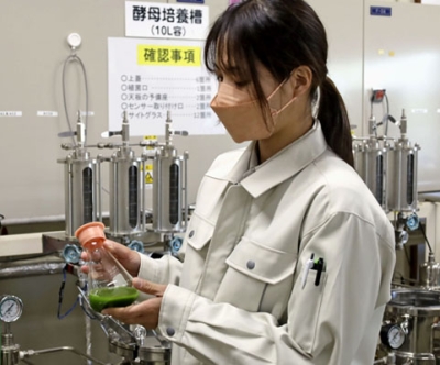 写真：糖蜜で藻を培養するフラスコを持つ近藤萌美さん＝帯広市