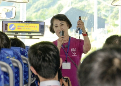 写真：北海道地震で大きな被害を受けた厚真町で、地震の経験を伝える現地ガイドを務める山内香さん。常に持ち歩く防災グッズを修学旅行の中学生に紹介した＝８月