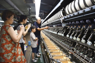 写真：碓氷製糸の自動繰糸機を見学するツアー参加者ら＝８月、群馬県安中市