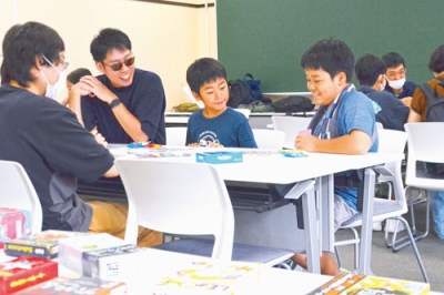 写真：学生とボードゲームを楽しむ家族連れ