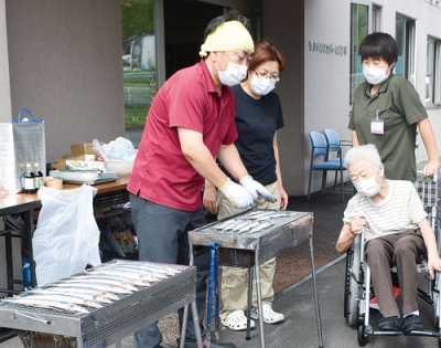 写真：入居者らに振る舞うサンマを炭で焼く佐藤施設長（手前）