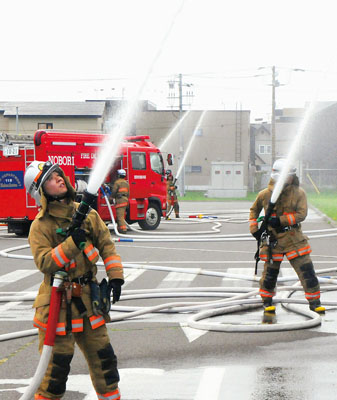 写真：消火訓練で工場建物へ放水する消防署員ら