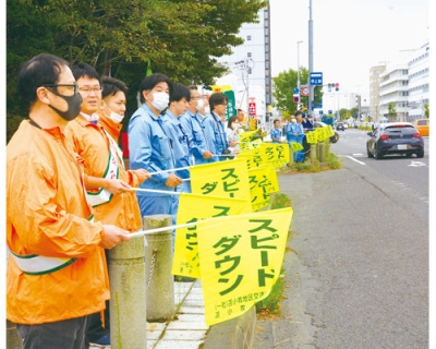 写真：「スピードダウン」と書かれた旗を掲げて無事故を訴える参加者