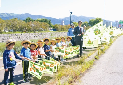 写真：国道沿いで旗を掲げ、ドライバーに交通安全を呼びかける堀井市長と京王幼稚園園児たち