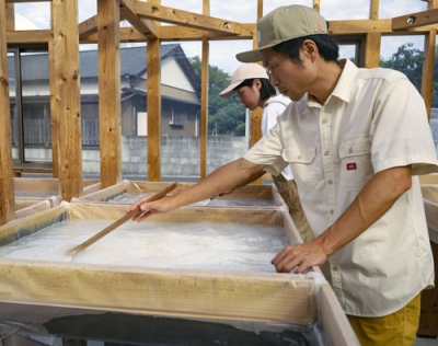 写真：製塩施設内で作業をする小坂英晃さん（手前）と千里さん夫婦＝１０月１２日、高知県安田町