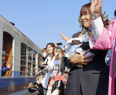 写真：会津鉄道芦ノ牧温泉駅の名誉駅長に就任し、駅長の小林美智子さんに抱かれて列車を見送るネコの「さくら」＝５日午前、福島県会津若松市