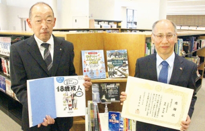 写真：感謝状を手にする林浩明専務取締役（右）と寄贈された本を持つ伊藤教育長