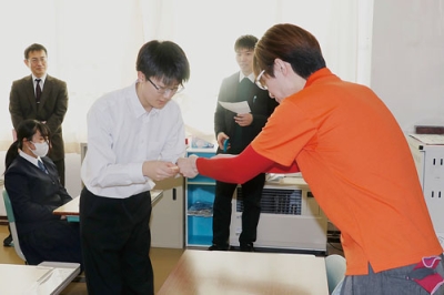 写真：矢島部長（右）から本を受け取る豊浦中の生徒（提供写真）