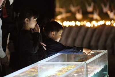写真：中華航空機墜落事故から３０年となり、慰霊施設「やすらぎの園」で水槽に花を浮かべる子どもたち＝２６日夜、愛知県春日井市