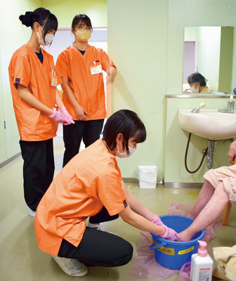 写真：看護師のアドバイスを受けながら患者の足浴を体験する高校生