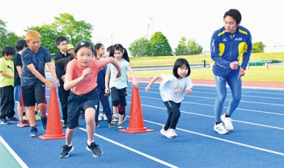 写真：現役の陸上選手のアドバイスを受けながらレーンを駆ける児童