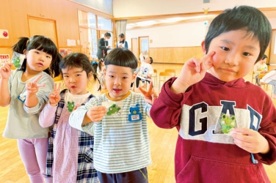 写真：佐々木さん夫妻が作ったカエルのお守りを手にする園児