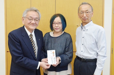 写真：目録を手渡す柴原事務局長（右）とマミネーさん（中央）