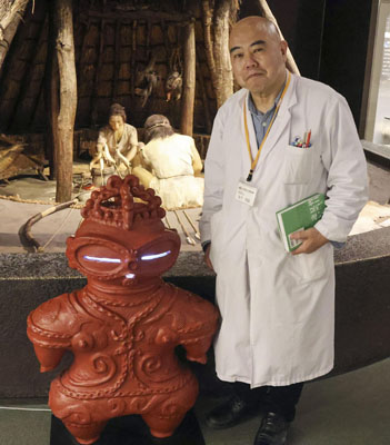 写真：金子昭彦さんと遮光器土偶のマスコット＝４月、盛岡市の岩手県立博物館