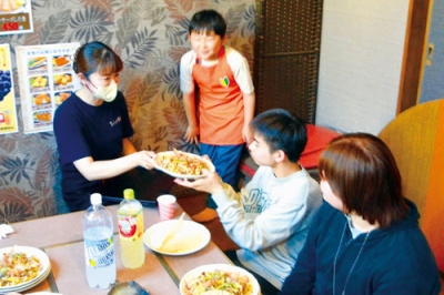 写真：施設の子どもたちや職員にお好み焼きとたこ焼きを振る舞う阿木村長（左）