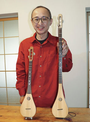 写真：３本弦の楽器「ミンミン」（右）と「ミンミン・ミニ」を前に笑顔の川合研さん＝名古屋市