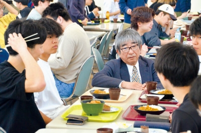 写真：特別価格メニューを食べる学生と会話する伊藤代表取締役（中央）