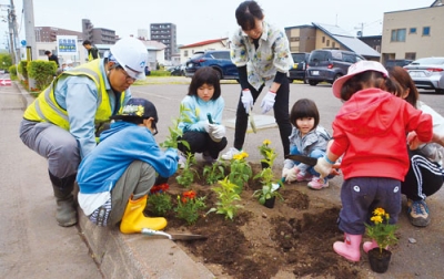 写真：本社前で花植え作業に取り組むメイセイ・エンジニアリングの社員と家族ら