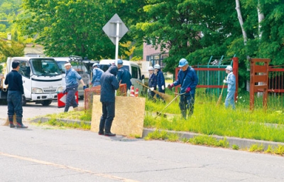 写真：道路の雑草を刈り取る組合員たち