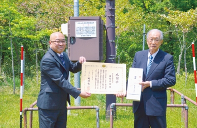 写真：観測所の前で感謝状を受け取った日野さん（右）