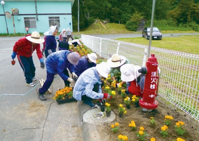 写真：会館近くの花壇に彩りを添える会員たち（提供写真）