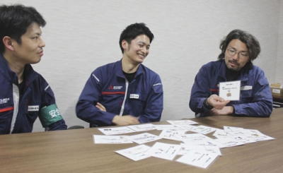 写真：部署間のコミュニケーション不足解消のため始まった「雑相の会」で使われる「話題カード」を手に、同僚と話す小林意弘さん（中央）ら＝３月、兵庫県赤穂市