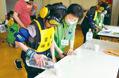 写真：コップに水を入れ、高齢者の日常動作を体験する生徒