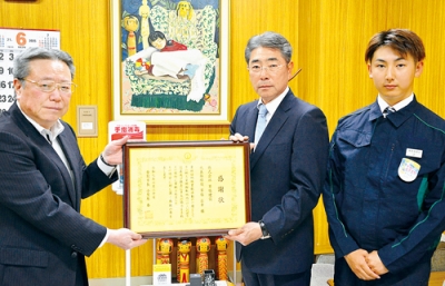 写真：安宅教育長（左）から感謝状を受け取る草塩代表取締役と新入社員の辻さん