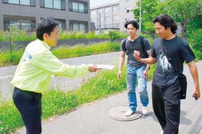 写真：学生に自賠責保険を紹介する啓発グッズを配る関係者