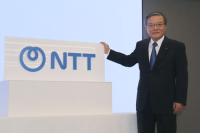 写真：「ＮＴＴ」への社名変更に伴う式典で、ロゴと写真に納まる島田明社長＝１日午前、東京都内