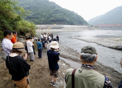写真：２０２０年７月の豪雨から５年となり、氾濫で多くの被害をもたらした球磨川（奥）周辺で黙とうする人たち＝４日午前、熊本県八代市