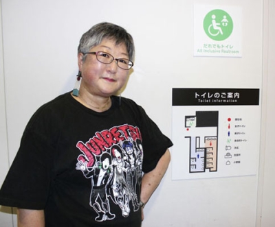写真：トイレの案内板の横に立つ百瀬まなみさん＝５月、東京都渋谷区