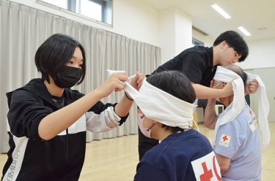 写真：けが人の頭にガーゼを巻いて止血する方法を学ぶ高校生