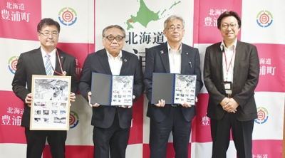 写真：贈られたフレーム切手を手にする杉谷町長（右から２人目）と金丸理事長（同３人目）