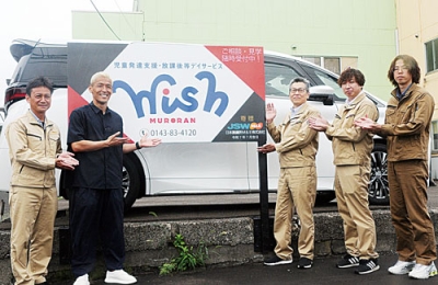 写真：「Ｗｉｓｈ室蘭」の看板前で記念撮影する菅野さん（左から２人目）と日鋼Ｍ＆Ｅの担当者ら
