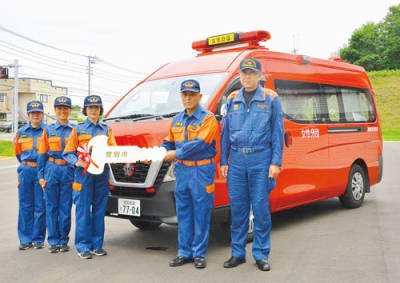 写真：パトライトやドアに「女性分団」が記された消防車両。野呂団長（右から２人目）からマスコットキーを受け取る渡辺分団長（同３人目）