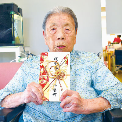 写真：「長寿祝金」の目録を手に百寿を喜ぶ橋本さん