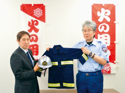 写真：ミニ防火衣を手渡す鈴木支部長（左）と受け取る沼田消防長