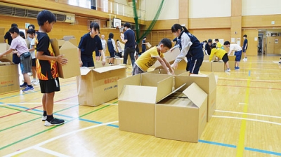 写真：中学生に教わりながらダンボールベッドを組み立てる児童ら