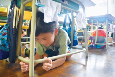 写真：机の下に素早く隠れ、地震発生時の対応を学ぶ虻田小１年生