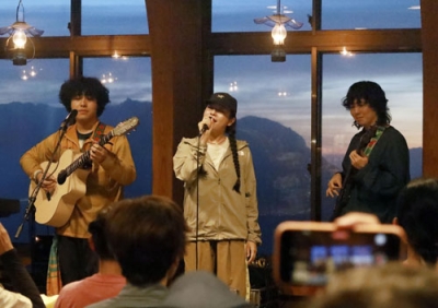 写真：夕焼けに染まった雲海を背にライブで熱演する「スーパー登山部」のＨｉｎａさん（中央）らメンバー＝８月、北アルプス白馬岳山頂付近の白馬山荘
